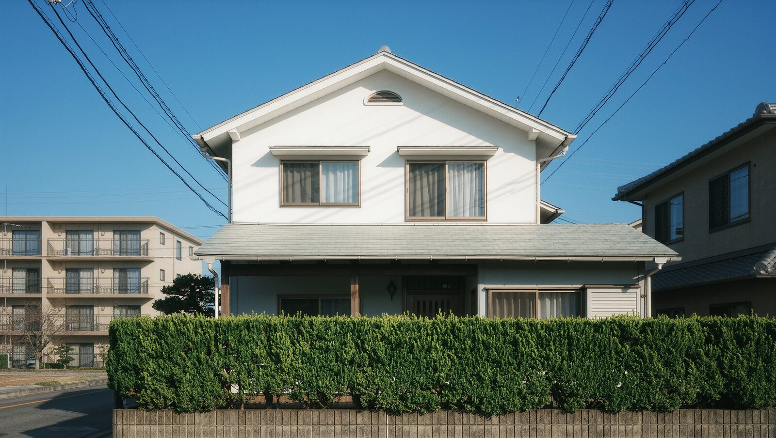 青空の下に建つ住宅街の白い二階建て戸建て